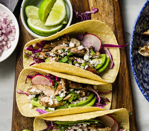 Stock photo of chicken fajita tacos with red cabbage, queso fresco, cilantro, avocado, radish and fresh squeezed lime.